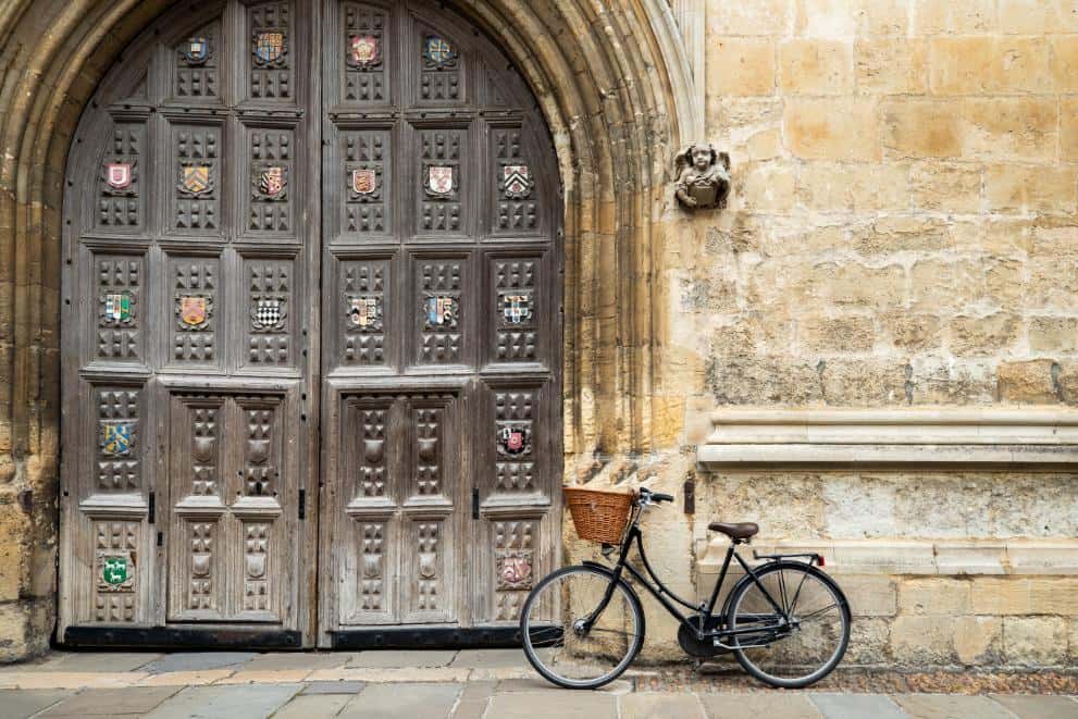 Vintage bicycle with basket on its handlebars parked beside a large medieval door in Oxford, part of the University of Oxford and an Oxford summer schools host venue