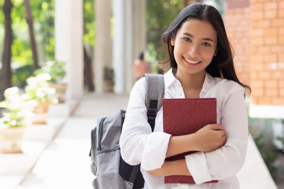 A female summer school student hugging a red study book and smiling